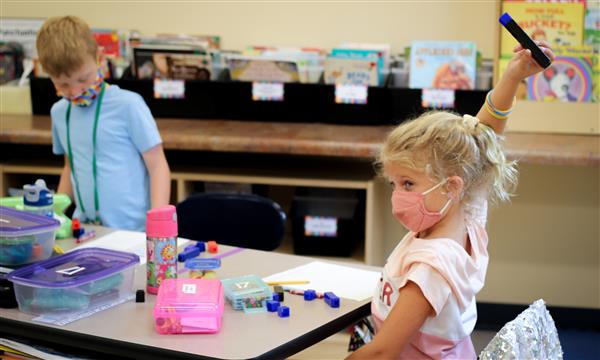girl raises her hand while sitting at her desk